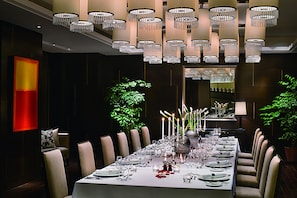 Ein langer Esstisch ist für ein festliches Essen gedeckt, umgeben von Stühlen, mit einem Chandelier über dem Tisch und einem großen abstrakten Gemälde an der Wand.