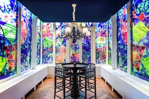 Une pièce dotée d’une table ronde et de chaises, d’un lustre et de vitraux aux couleurs vives.