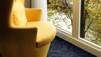 Un sillón amarillo junto a una ventana con vistas a un árbol y edificios.