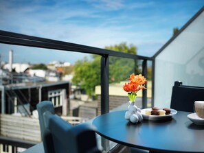Un balcon avec une table, un vase rempli de fleurs et une assiette avec des biscuits et une tasse.