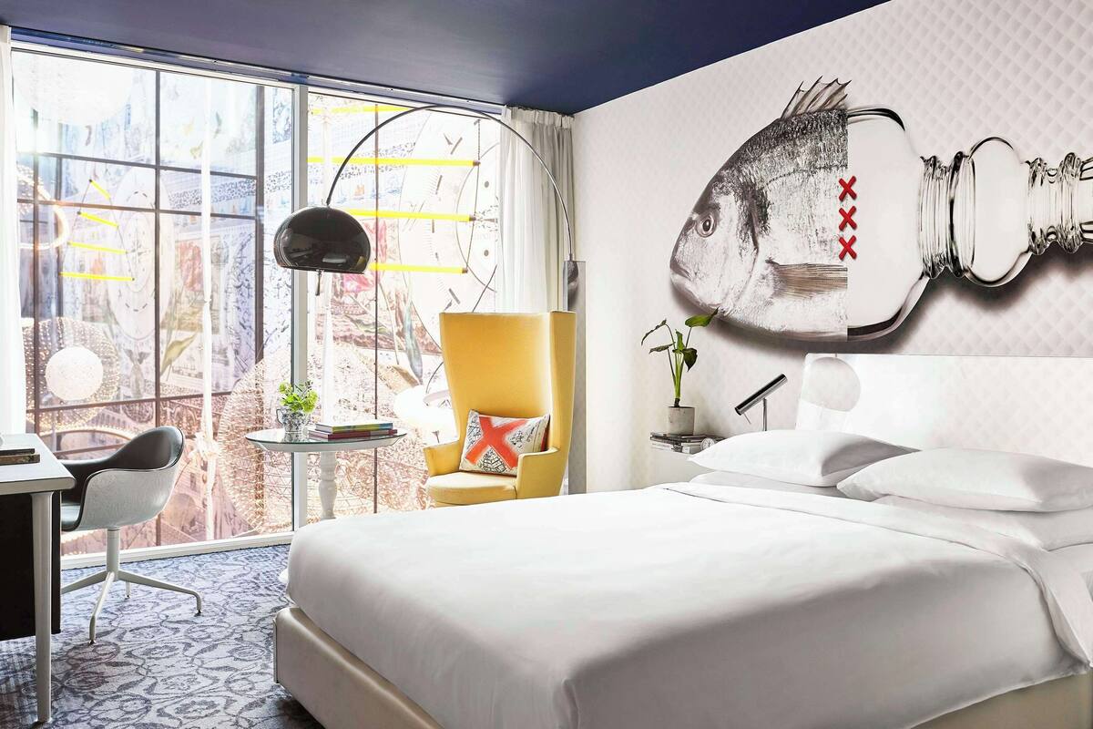 Habitación de hotel con una cama grande, un escritorio, una silla, una mesita con una planta y una obra de arte en la pared.