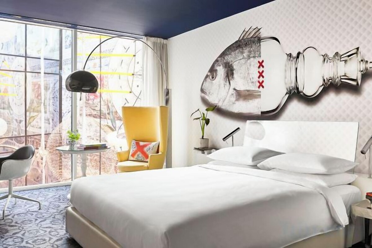 A hotel room with a large bed, a chair, a small table, and a window with a view.