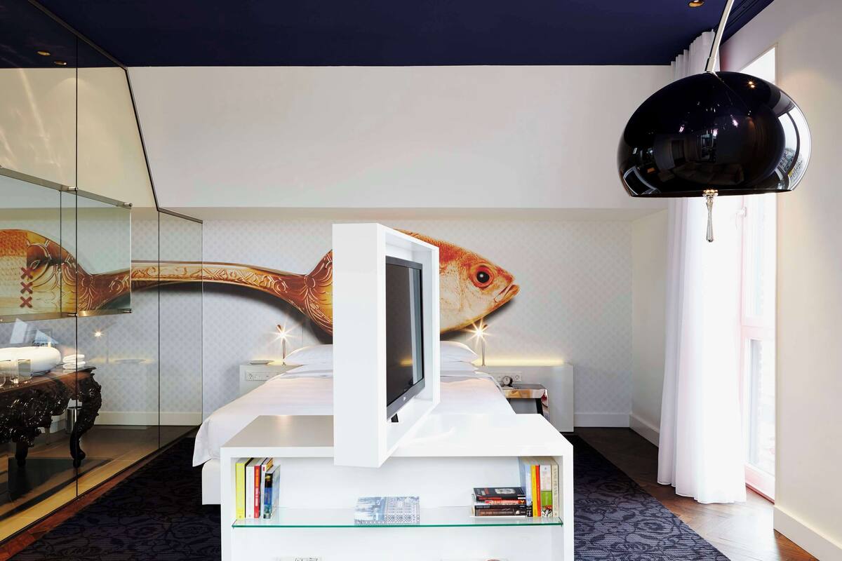 Una habitación moderna con un gran mural de peces, una mesita de noche blanca con televisor y una lámpara colgante negra.
