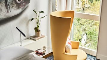 Una habitación moderna con un ventanal grande, una silla amarilla, una mesita y una estantería.