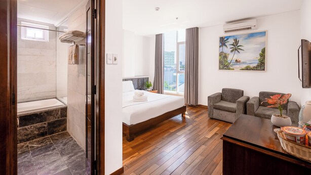 A hotel room with a bathroom, a bed, a seating area, and a painting on the wall. - Tarasa Hotel (Da Nang)