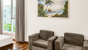 A modern hotel room with a wooden floor, two grey armchairs, a painting of a beach scene, and an air conditioning unit on the wall. - Tarasa Hotel (Da Nang)