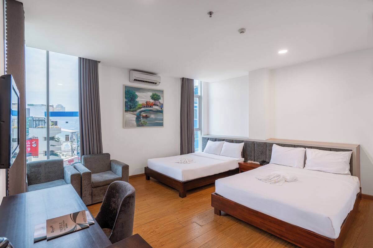 Habitación de hotel con dos camas, un escritorio, una silla y un ventanal con vistas a la ciudad.