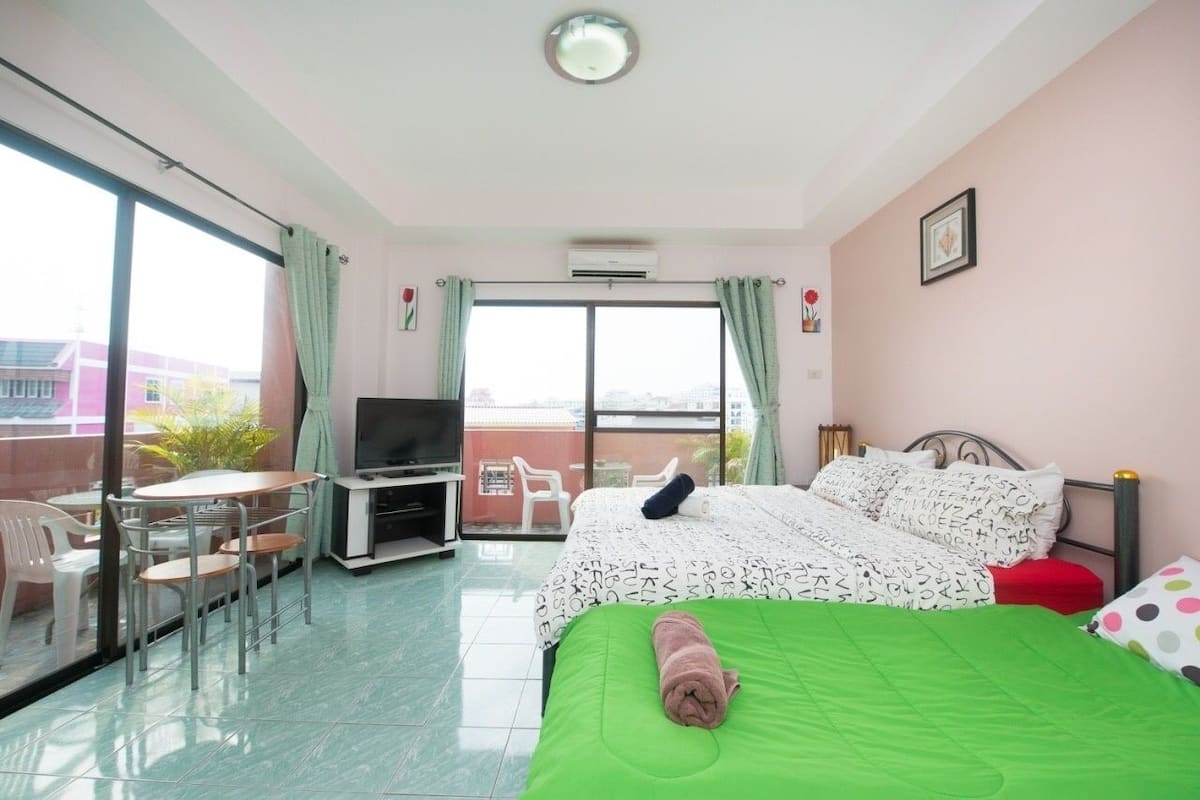 A hotel room with a bed, a TV, a balcony with chairs, and a table.