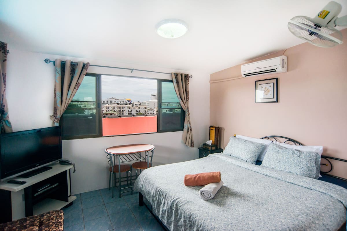 A hotel room with a bed, a TV, a small table, and a window with curtains.