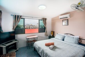 A hotel room with a bed, a TV, a small table, and a window with curtains. - Pattaya Holiday Lodge (Pattaya)