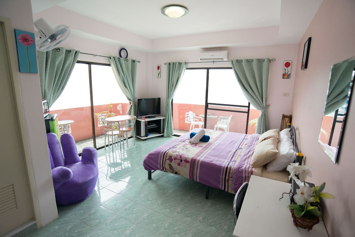 A hotel room with a bed, a chair, a desk, a TV, and a balcony with a table and chairs.