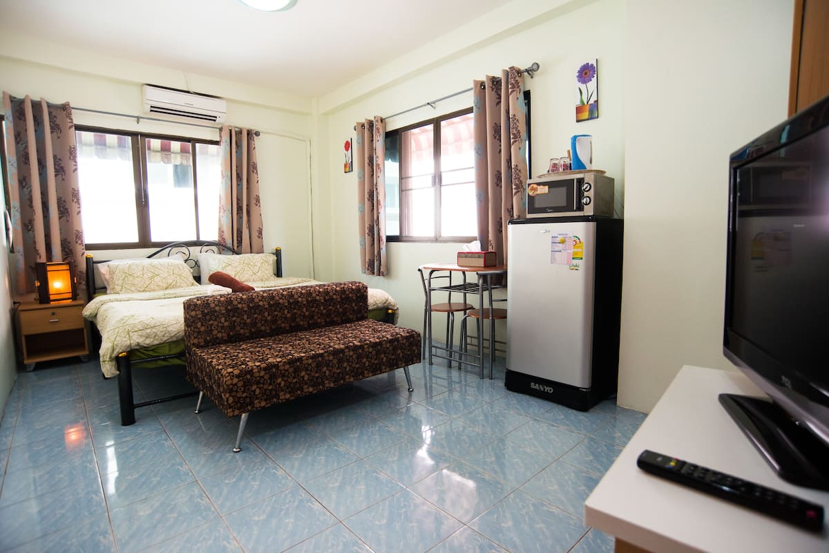 A compact hotel room with a bed, sofa, TV, microwave, and a small dining area.