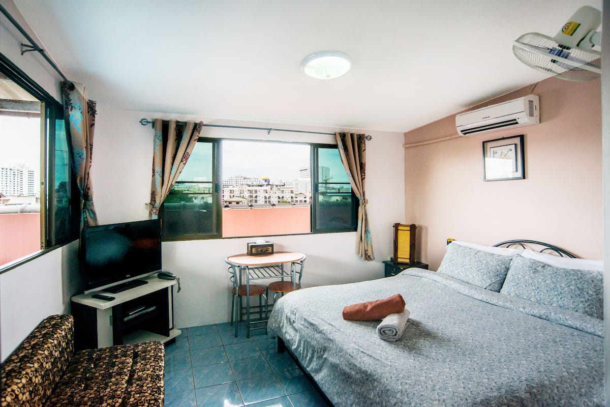A hotel room with a bed, a TV, a small table, and a window with curtains.