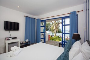 A hotel room with a bed, a TV mounted on the wall, a desk with a lamp, and a view of the sea through an open door. - Kerala Coco Resort (Rayong)