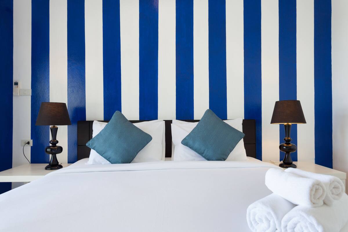A hotel room with a bed, two nightstands, two lamps, and a striped wall.
