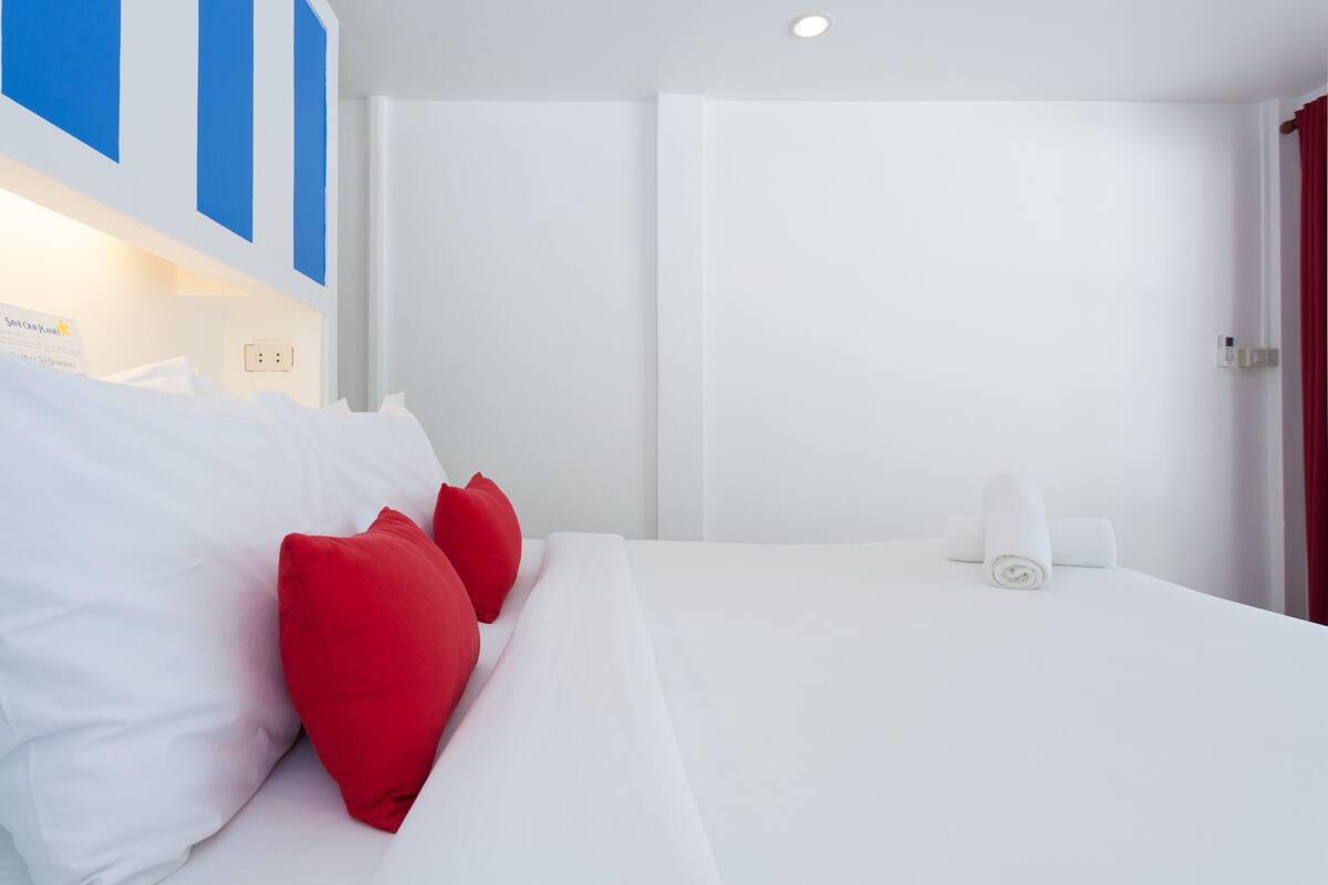 A hotel room with a bed, white bedding, red pillows, a white towel, and a blue and white wall design.