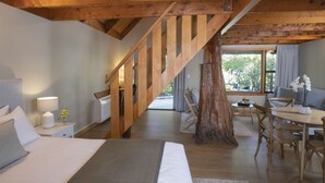 A bedroom with a wooden staircase, a bed, a nightstand, a lamp, and a window with a view of the outdoors. - Awaroa Lodge (Awaroa Bay)