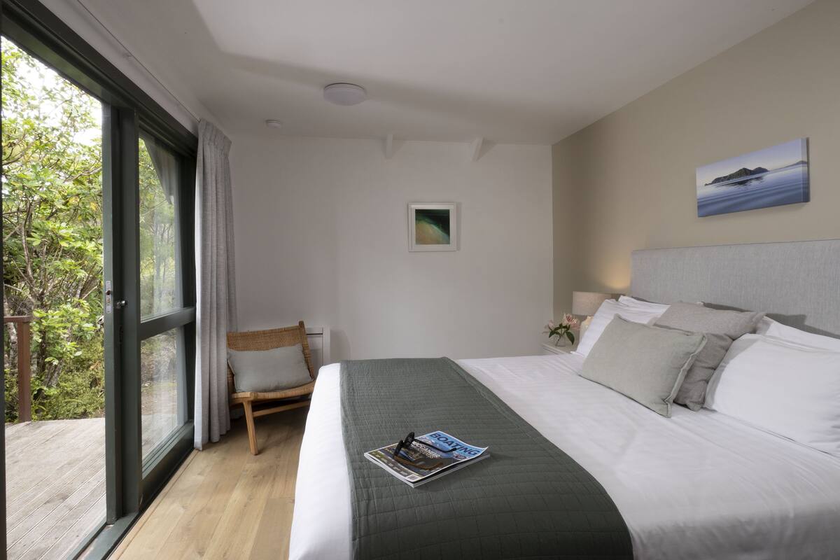 A bedroom with a large bed, a small chair, a window, and a painting on the wall.
