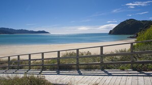 Ein hölzerner Steg führt zu einem Strand mit klarem, blauem Wasser und sanften Hügeln in der Ferne.