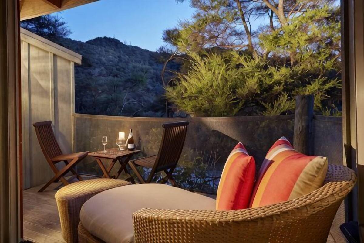 A balcony with wicker furniture, a table with glasses, and a view of trees and hills.