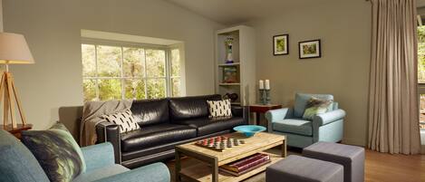 Una sala de estar moderna con un sofá de cuero negro, un sillón azul y una mesa de centro de madera con un juego de ajedrez.