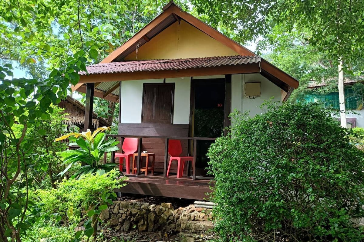 A small, single-story building with a porch, surrounded by lush greenery.