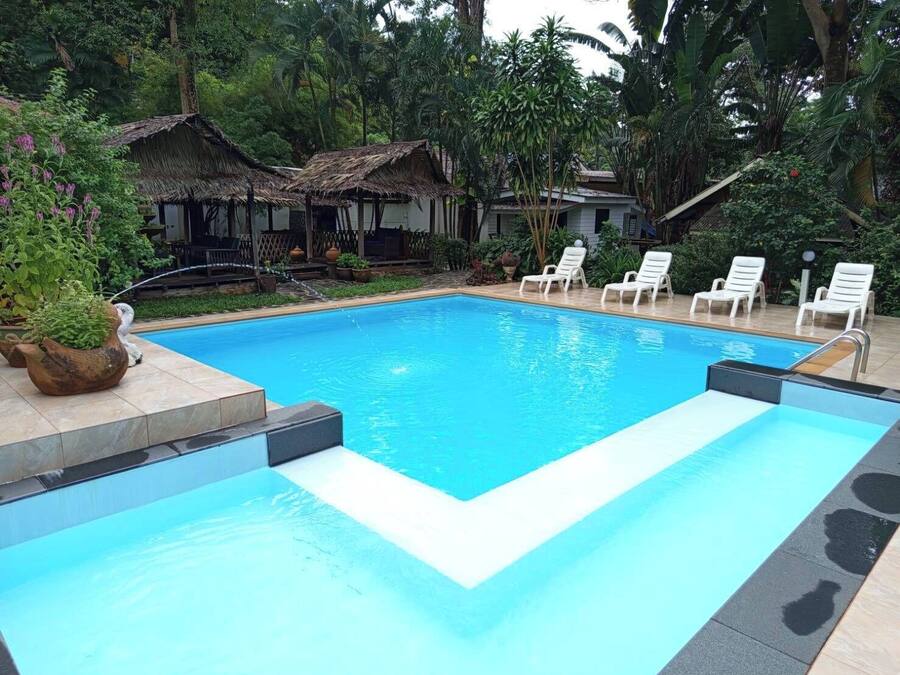 Una piscina rettangolare con acqua cristallina blu e un bordo piastrellato, circondata da lettini bianchi e piante in vaso.