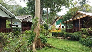 A lush garden with a large tree, wooden houses, and a well-maintained lawn. - Faye Orchid Resort (Ko Chang)