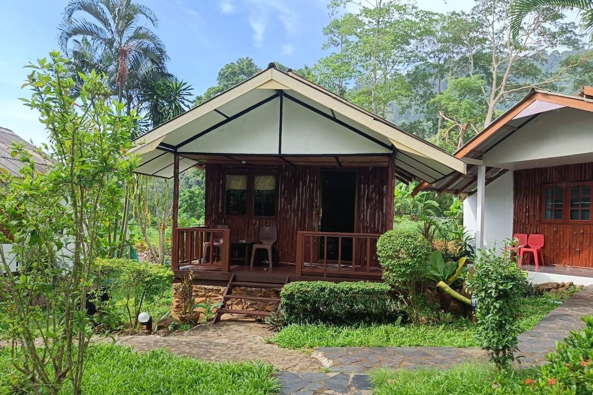 A rustic wooden house with a porch, stone pathway, and lush greenery.