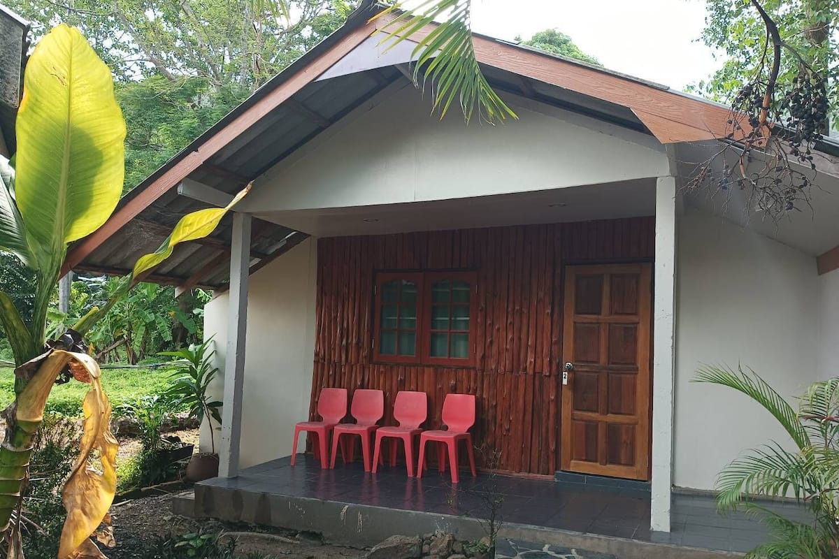 A small building with a porch, wooden door, and three red plastic chairs.