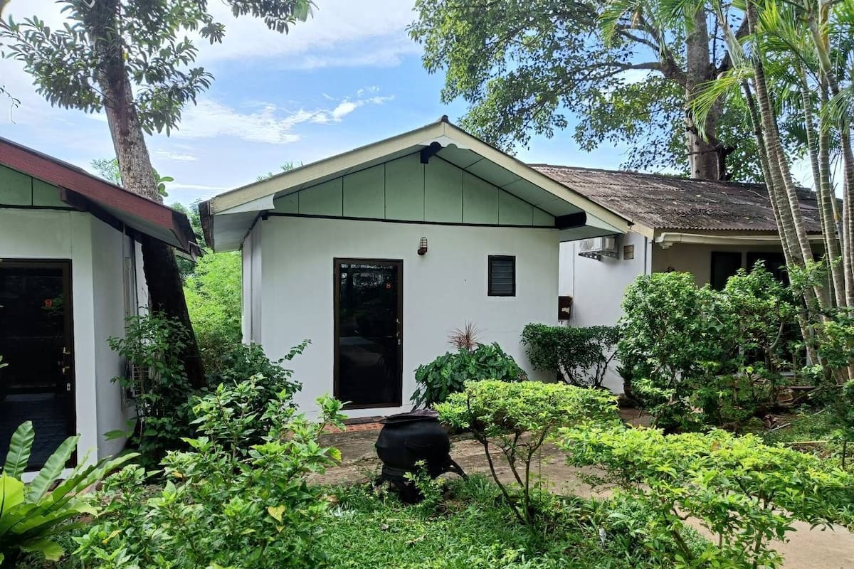A white building with a black door and a small window, surrounded by lush greenery.