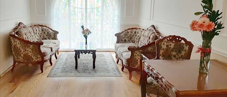 A room with two upholstered chairs, a small table, and a vase with flowers.
