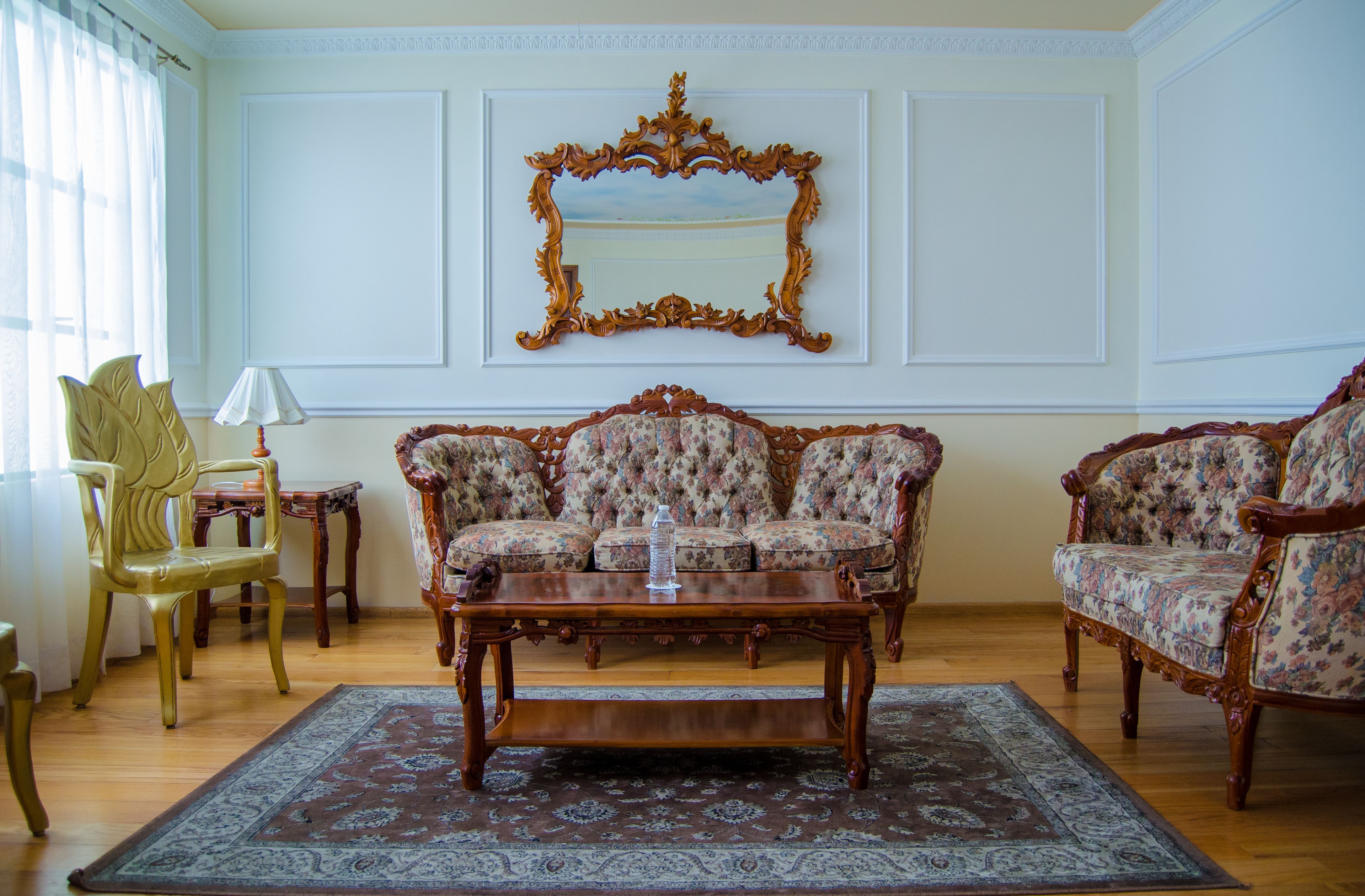 A room with a floral sofa set, a wooden coffee table, and a large ornate mirror on the wall.