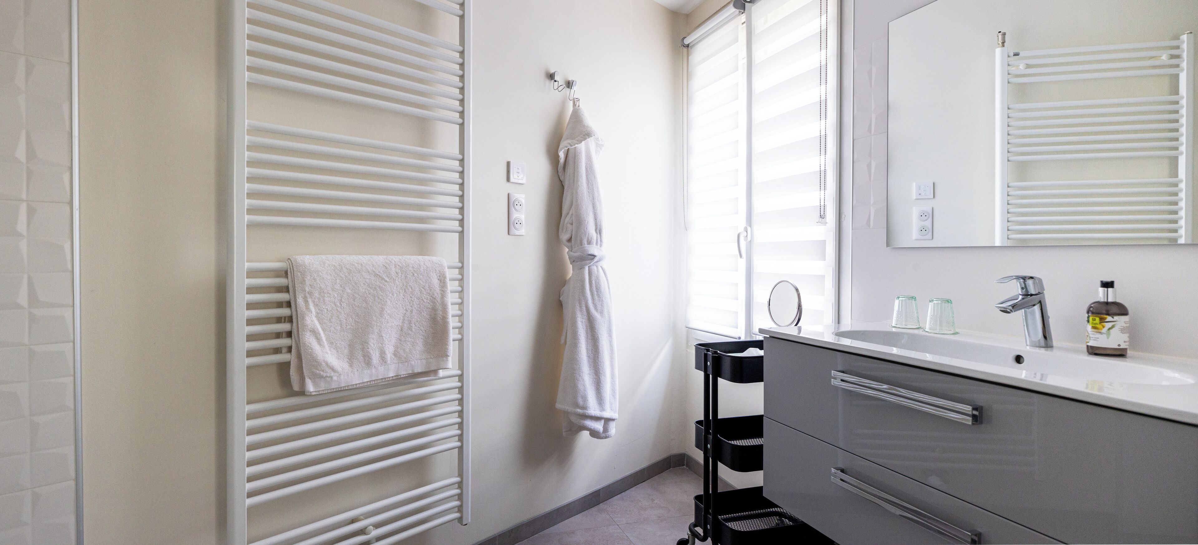 A modern bathroom with a white towel rack, a black towel rack, a white sink with a mirror, and a black trash bin.