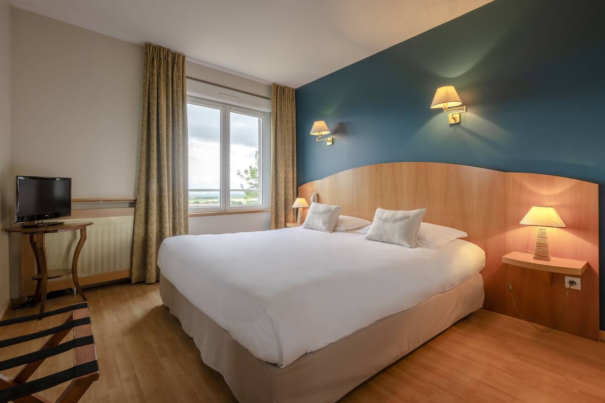 A hotel room with a large bed, a television on a small table, and two wall-mounted lamps.