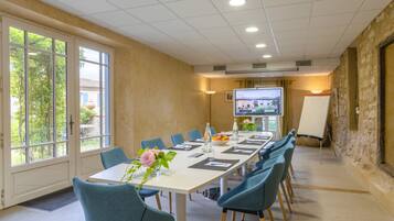 A conference room with a long table, blue chairs, a projector screen, and a whiteboard.