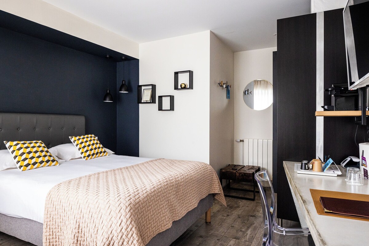A modern bedroom with a large bed, bedside lamps, a desk with a computer, and a television.