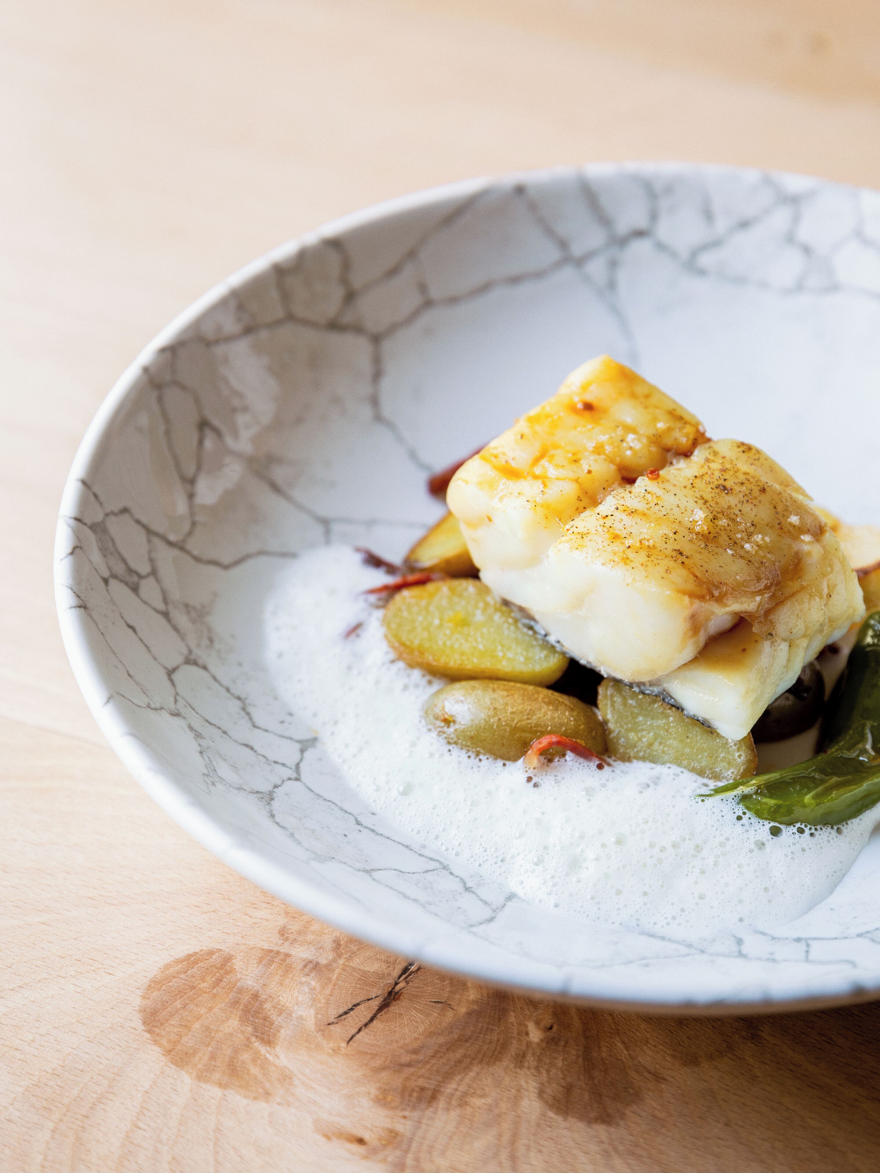 A bowl with a piece of fish, potatoes, and a creamy sauce.