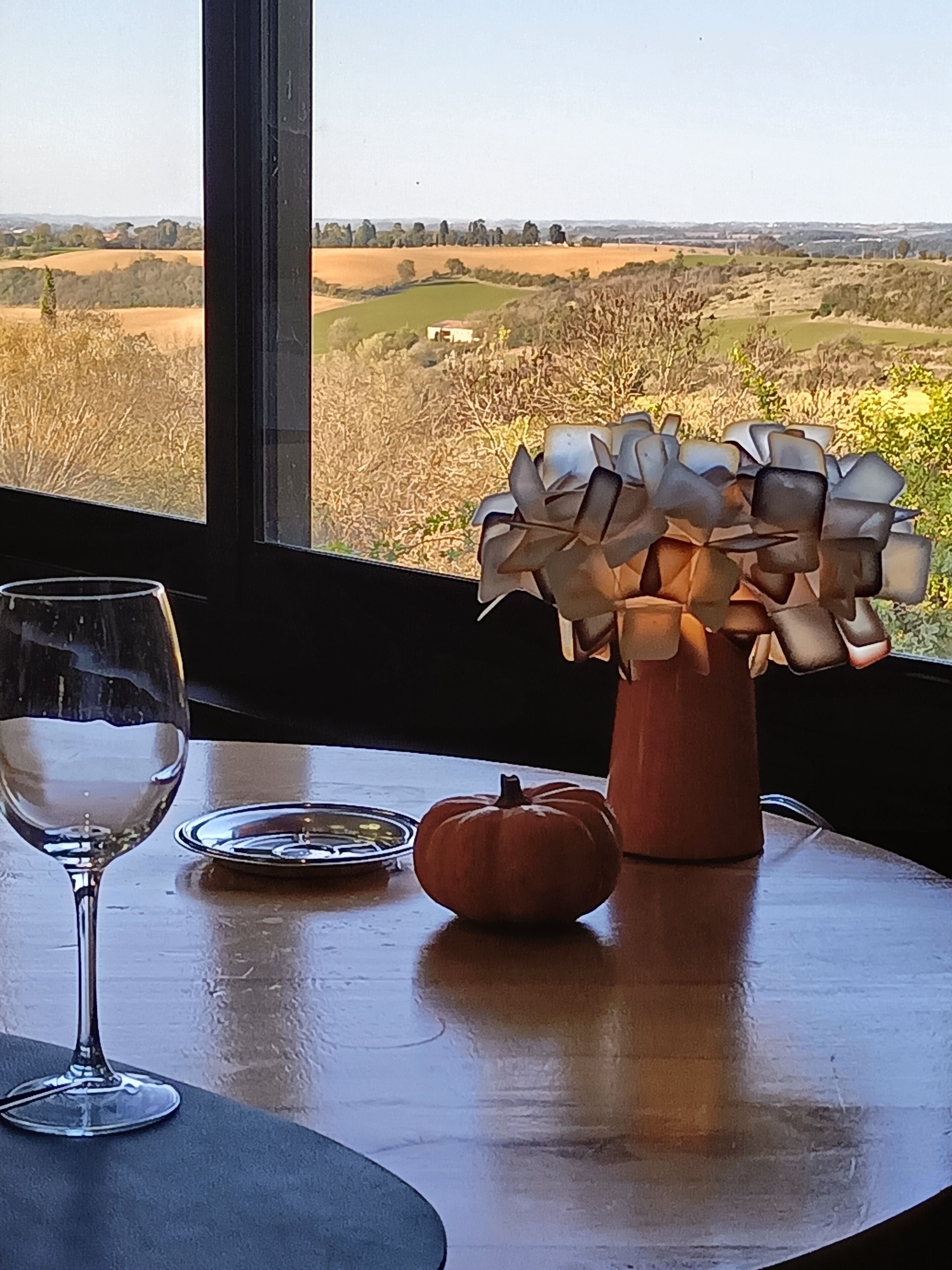 A table with a vase of flowers, a pumpkin, and a wine glass.