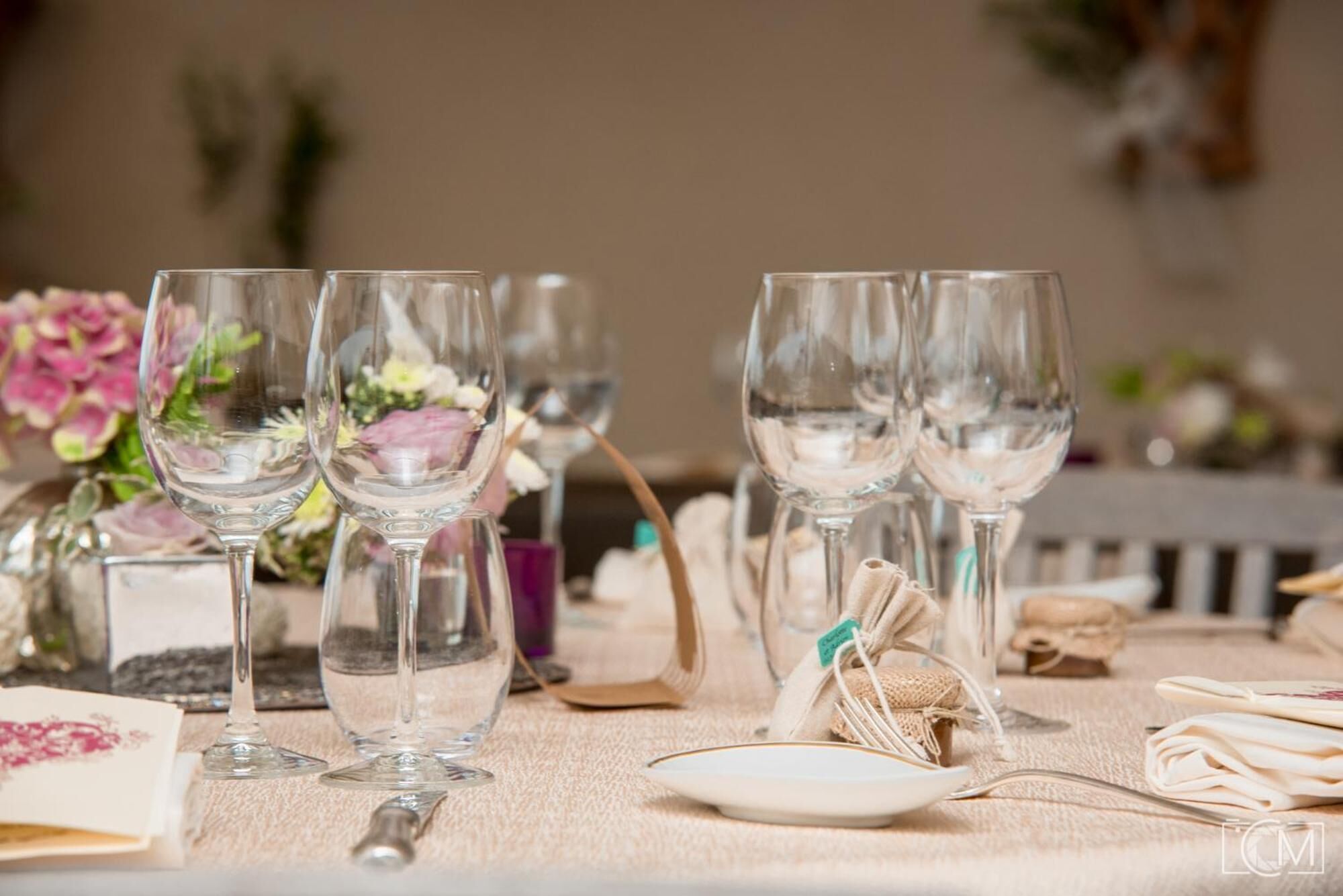 A table set with wine glasses, a plate, and a spoon, with a floral arrangement in the background.