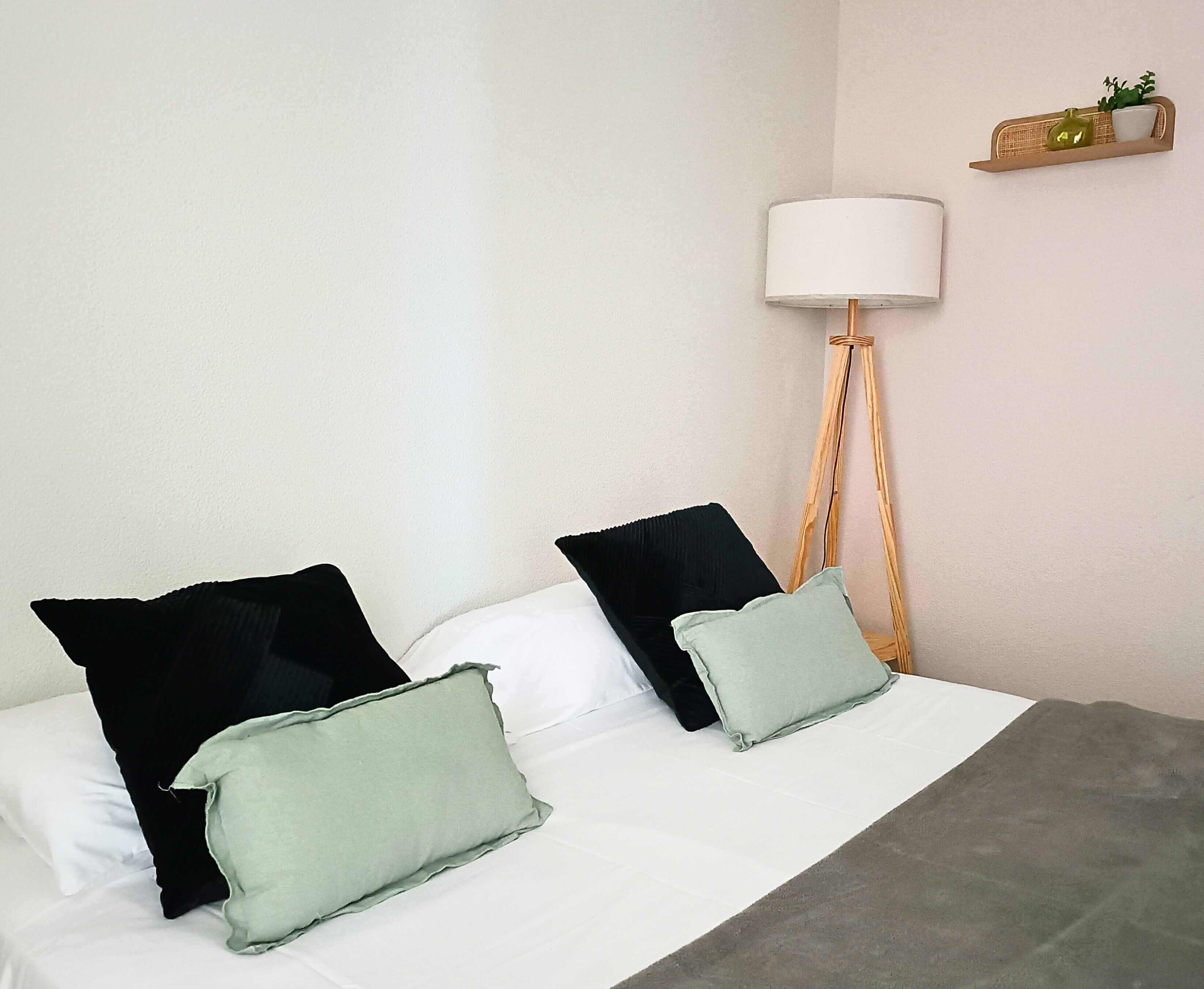 Ein Bett mit schwarz-weißen Kissen, einer grauen Decke und einer Stehlampe mit einem weißen Lampenschirm.
