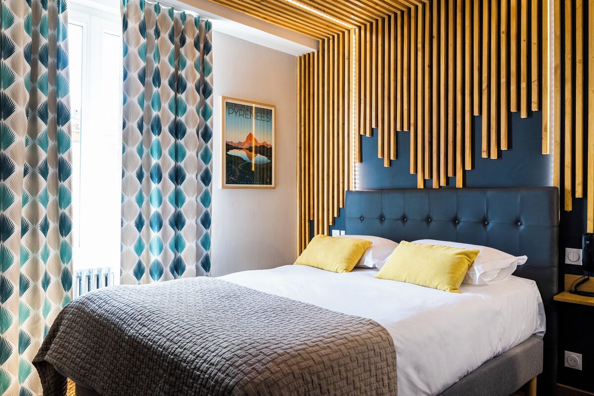 A modern hotel room with a large bed, wooden slats on the wall, and a view of the mountains.