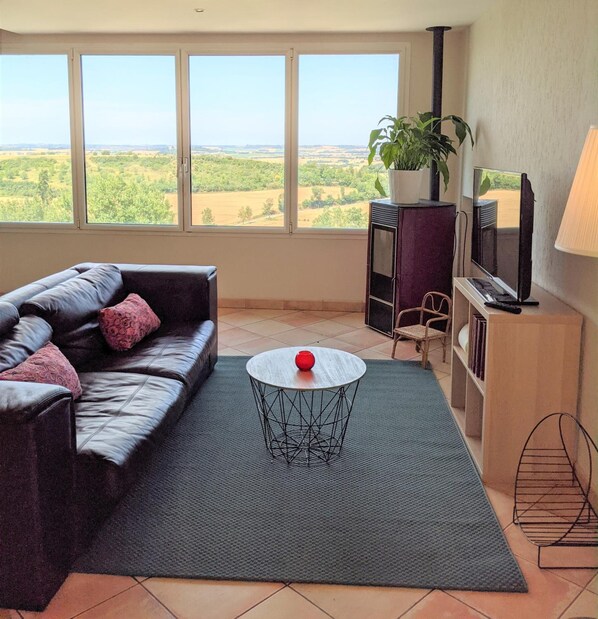 A living room with a leather sofa, a round coffee table, a TV, and a large window with a view of the countryside. - Auberge du Poids Public (Saint-Felix-Lauragais)