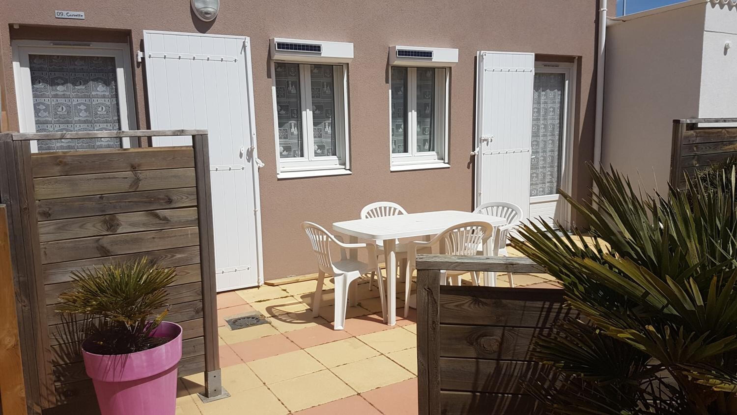 A patio area with a white table and chairs, a wooden gate, and potted plants.