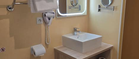 Un baño con inodoro, lavamanos, toallero y dos espejos.