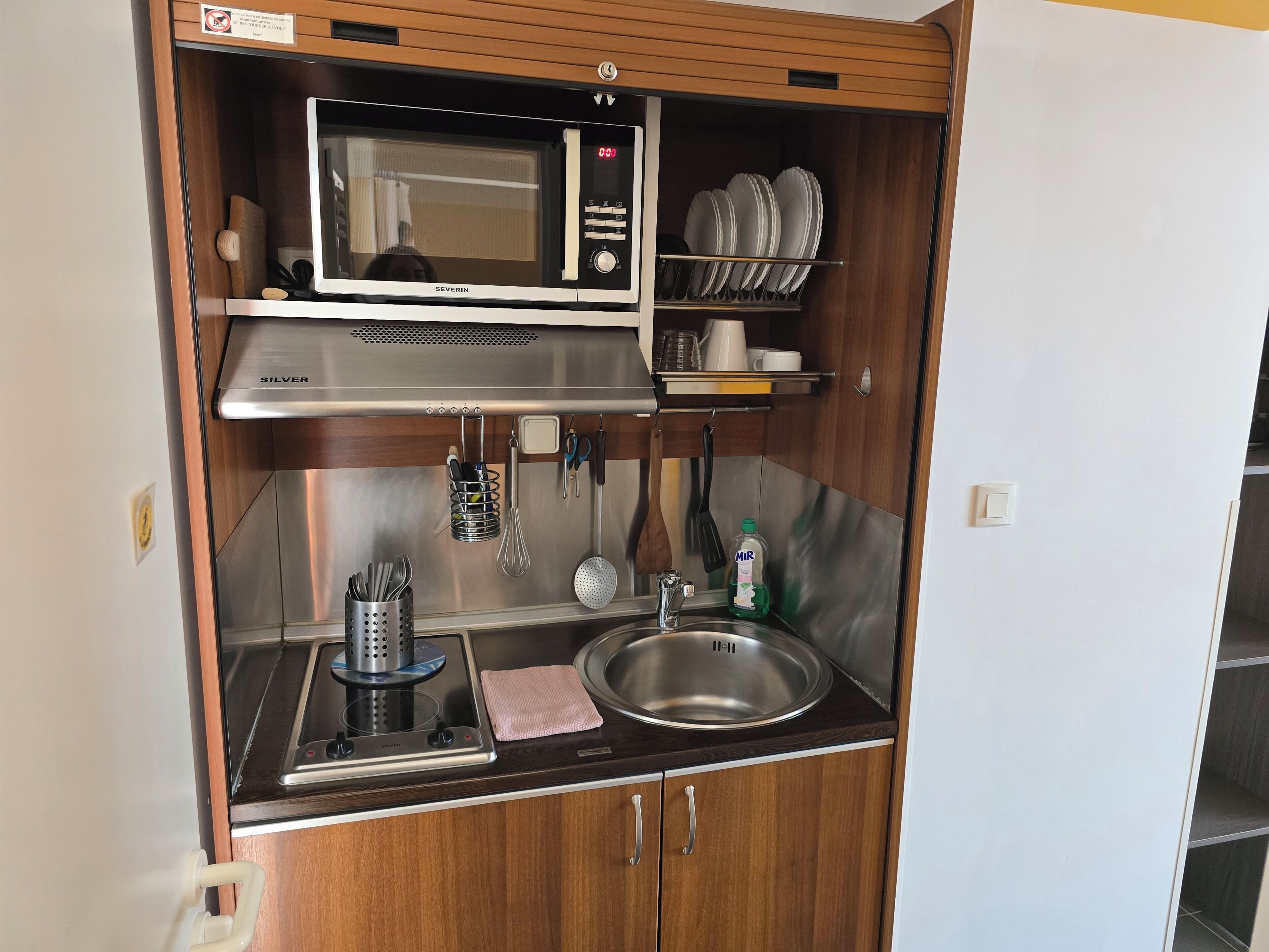 A compact kitchenette with a microwave, sink, and utensil holder.