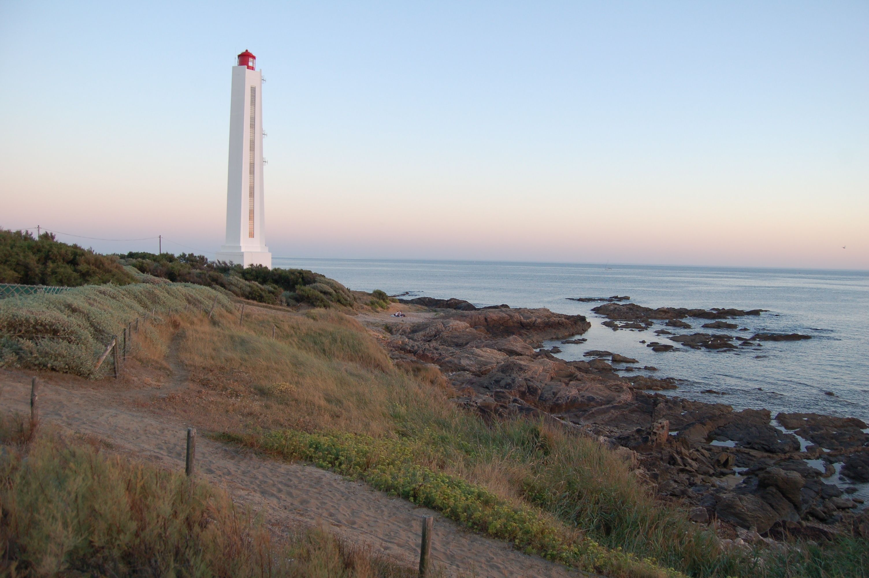 Paesaggio costiero con un faro, un litorale roccioso e terreno erboso.