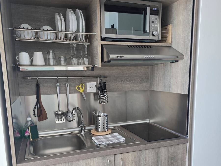 A compact kitchen with a microwave, sink, and utensil storage.