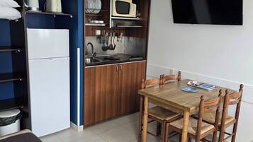A compact kitchen with a microwave, stove, and sink, a dining table with chairs, and a TV mounted on the wall.
