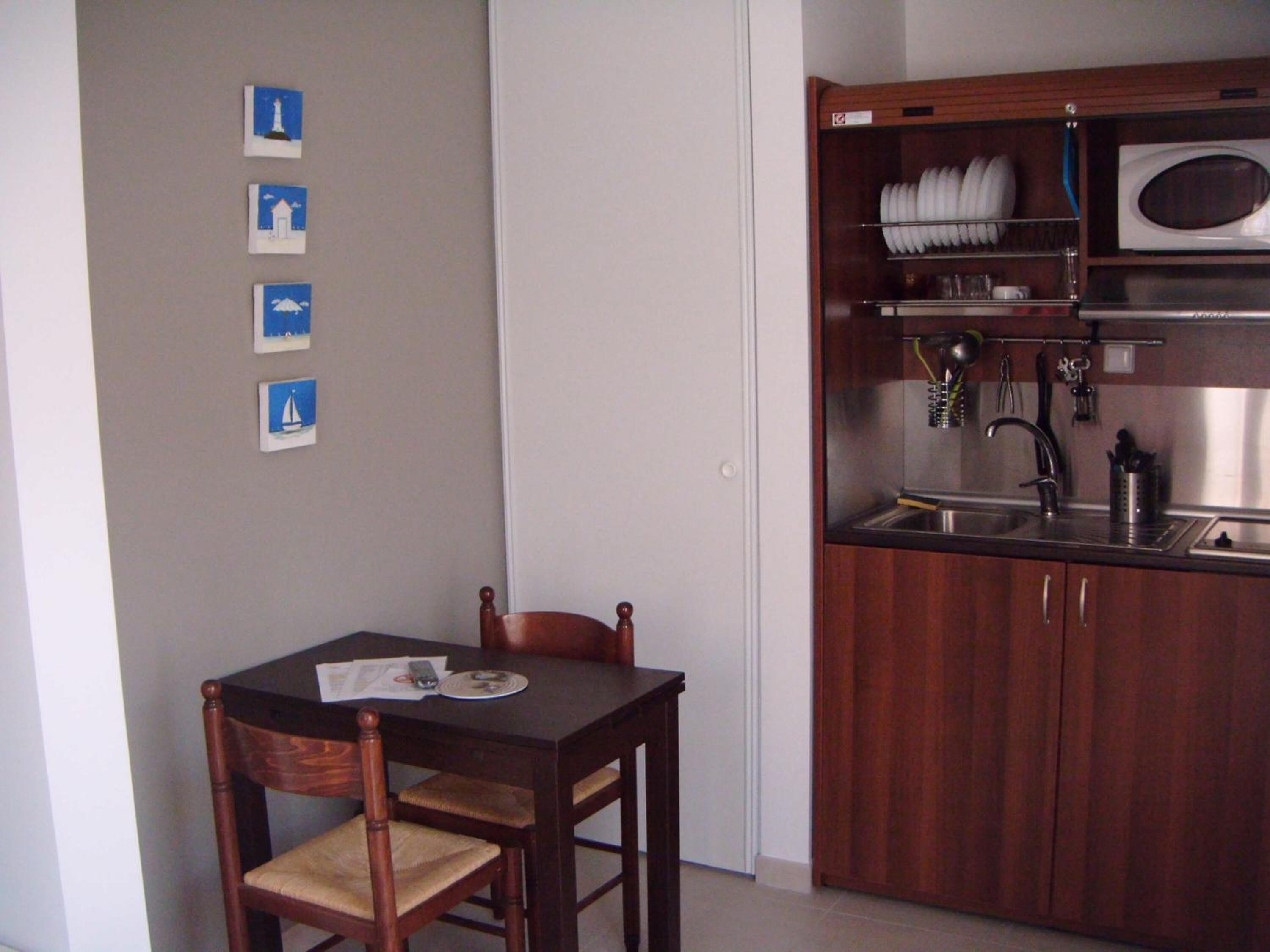 Cocina compacta con microondas, lavamanos y utensilios. Una mesa de madera con una silla está ubicada frente a la cocina.